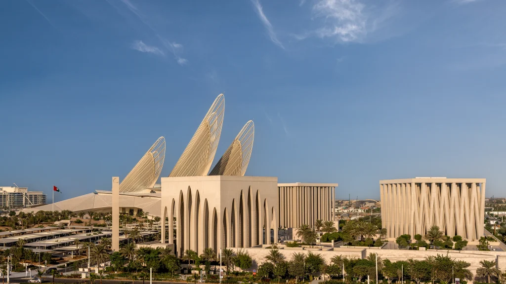Aerial architectural photograph by Deed Studio showing Saadiyat Island in Abu Dhabi, including the Abrahamic Family House, Louvre Abu Dhabi, Zayed National Museum, Guggenheim Abu Dhabi, Natural History Museum Abu Dhabi, and teamLab Phenomena, illustrating the spatial relationship between the cultural institutions.